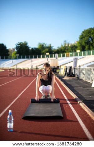 Athlete girl twists her mat after playing sports on a sunny summer day at the stadium.