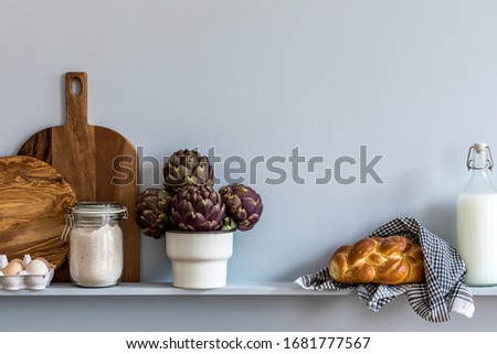 Modern composition on the kitchen interior with wooden cutting board, milk, bread, eggs and kitchen accessories in stylish home decor.