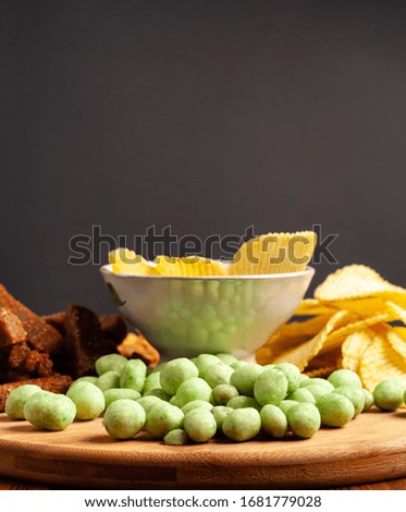Assorted dry snacks on a wooden board. Chips, peanuts, croutons, wasabi.