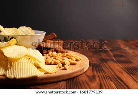 Assorted dry snacks on a wooden board. Chips, peanuts, croutons, wasabi.