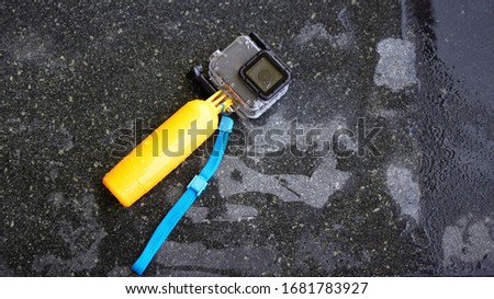 action camera with waterproof case and float stick on poolside of swimming pool on blur kid in water background in summer beach holiday concept