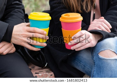 two girls sitting outdoors holding coffee cup on a city street background, take away coffee.Breakfast on the go.Sustainable lifestyle concept.reusable travel mug. Zero waste. 