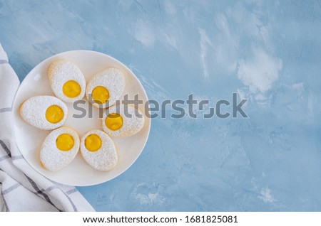 Easter cookies in the form of Easter egg with powdered sugar and lemon cream on a white plate on a light blue concrete background. A greeting card. Easter background. Horizontal, Copy space. Top view