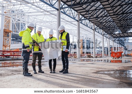 Group of engineers with blueprints standing on construction site.
