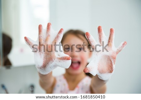 Little girl washing hands with water and soap in bathroom. Happy kid showing soapy palms. Hands hygiene and virus infections prevention. 