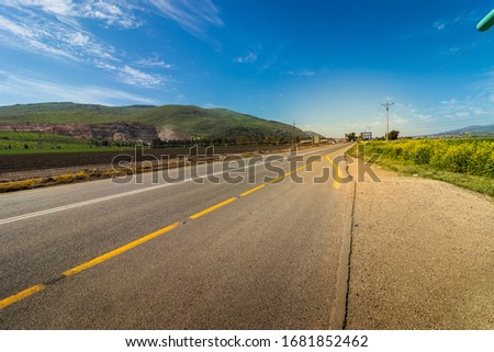 Asphalt road painted in white and yellow surrounded by green field and yellow wildflowers wide angle photography
