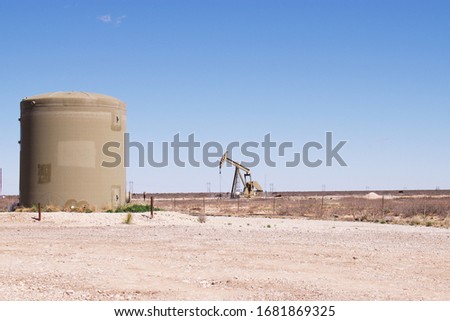 Single Pump-jack in distance with water tank in foreground. 