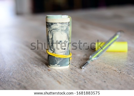 Dollars rolled up and tied with a yellow rubber band. Nearby lies a medical thermometer. Concept - paid medicine, illness