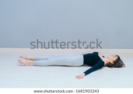 Beautiful young woman working out at home, doing yoga exercise on wooden floor, lying in Shavasana Corpse or Dead Body Posture , resting after practice, meditating, breathing. Full length, top view Royalty-Free Stock Photo #1681903243