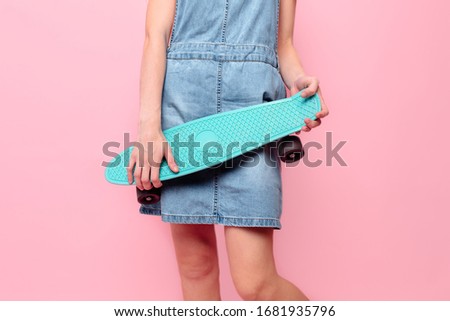 Close- up of a girl holding a skateboard on an isolated pink background