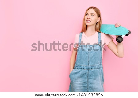 Portrait of a stylish attractive girl smiling and holding a skateboard isolated on a pink background in the Studio