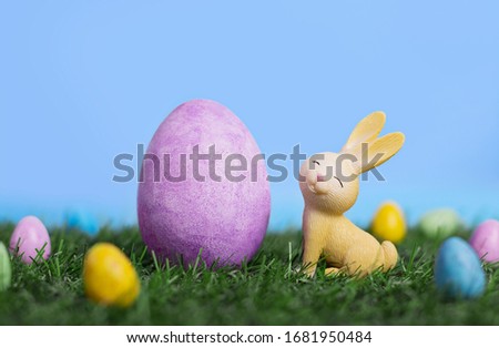 Cute little cartoon easter bunny sitting on grass among easter eggs in the garden, easter banner