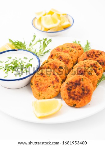Fish cakes on a plate with lemon wedges, salad and sauce. Side view white background.