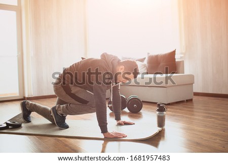 Young ordinary man go in for sport at home. Picture of real ordinary man doing abs exercising by running on one place with legs. Worksout freshman warming up body. Stretching alone in sunny apartment Royalty-Free Stock Photo #1681957483