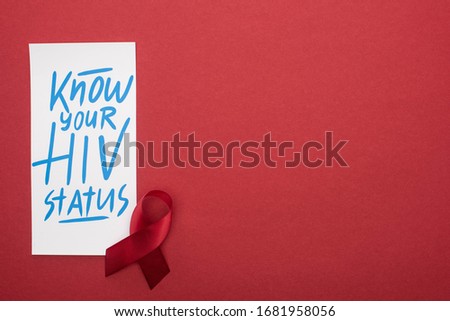 top view of card with know your HIV status lettering and awareness ribbon on red background
