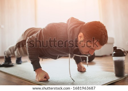 Young ordinary man go in for sport at home. Stand in plank position on his fists or doing push ups exercising. Hardworking beginner or ordinary man improving his body. Start workout without trainer Royalty-Free Stock Photo #1681963687