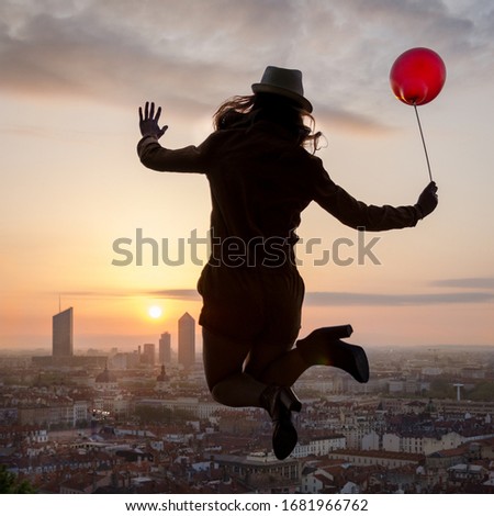 Woman jumping with balloon in front of Lyon skyline at sunrise with a balloon