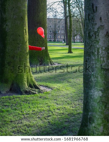 Someone hiding behind a tree wtih only one hand and a balloon visible