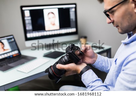 Handsome photographer holding his camera smiling at camera in creative office