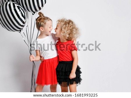Happy kids girls sisters in red and black skirts celebrate birthday are screaming singing songs playing celebrating having fun at party with stylish air balloons on white