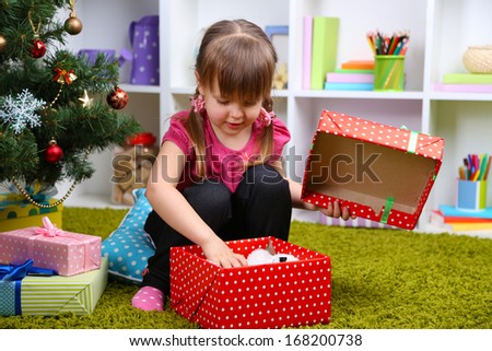 Little girl with present box near Christmas tree in room