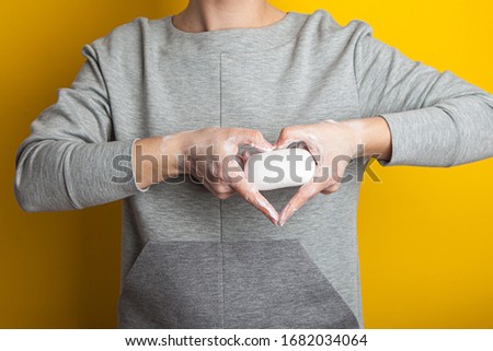 Female hands making sign Heart by fingers holding a bar of soap. washing hands with soap saves life and protects against covid-19. Hand disinfection during quarantine . yellow background, studio