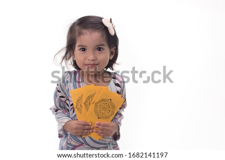 A female child wearing traditional "baju kurung",holding a packet money also known as "duit raya",isolated over white. Eid cocept.