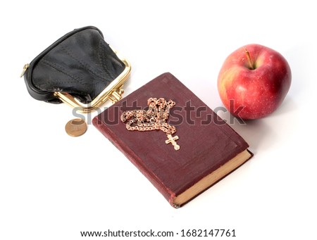 a ripe apple next to a purse with a metal coin and a religious book with a golden cross