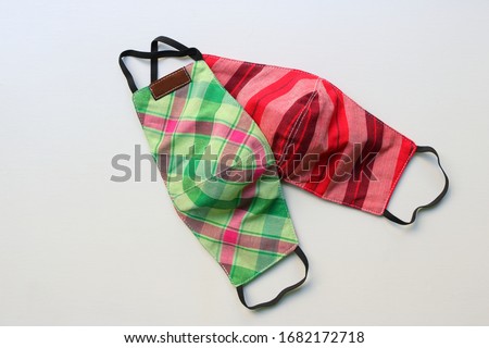 Two handmade face masks made from plaid cloth placed on wooden table, washable and reusable, can be used during shortage of surgical mask due to coronavirus pandemic   Royalty-Free Stock Photo #1682172718
