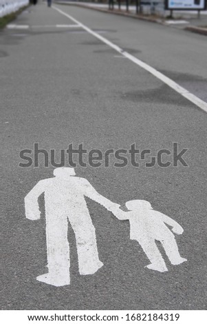 Walking man or woman and child pavement sign painted white on a concrete way 
