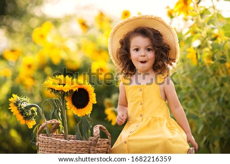 
little curly girl in a hat in a field of sunflowers Royalty-Free Stock Photo #1682216359