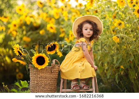
little curly girl in a hat in a field of sunflowers Royalty-Free Stock Photo #1682216368