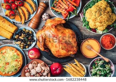 Roasted whole chicken, rice, pumpkin, corn, honey, nuts, vegetable salads over wooden background. Top view, copy space. Autumn harvest, organic vegetables. Autumn family dinner. Food concept