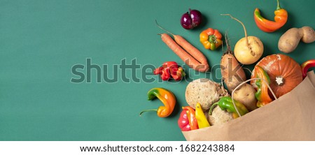 Trendy ugly organic vegetables. Assortment of fresh eggplant, onion, carrot, zucchini, potatoes, pumpkin, pepper in craft paper bag over green background. Top view. Cooking ugly food concept. Non gmo Royalty-Free Stock Photo #1682243884