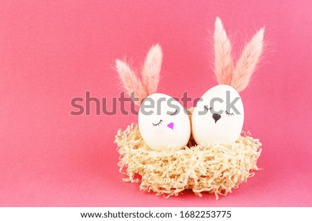 Easter eggs in a nest of decorative paper. white eggs in the form of bunnies with cute faces and fluffy ears. eggs on a pink background for Easter