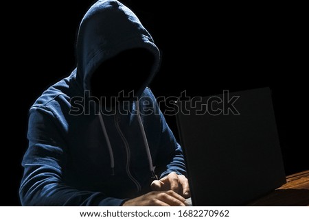 Hacker with computer man sitting at a table in a hood