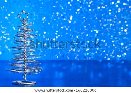 close-up of metallic modern christmas tree on wood table on blue tint light bokeh background with space for text