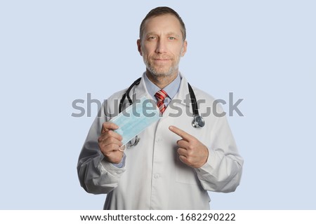 A doctor in a medical coat and a stethoscope on his shoulders shows a medical mask