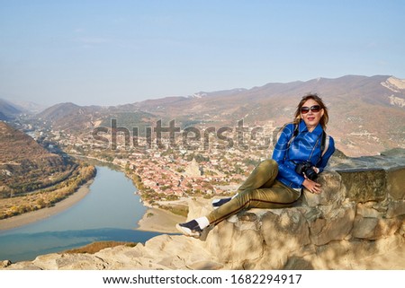 Attractive beautiful young girl who is female photographer traveller holding modern mirror camera in the hands outdoors and mountains valley in background
