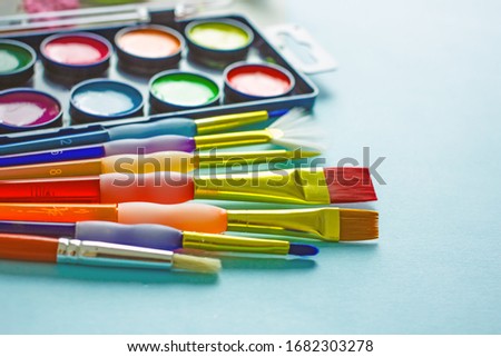 Brushes and paints on a light background. Watercolor brushes of different colors in the background watercolor paints. Background about creativity, hobbies, needlework. The concept of free time, hobby