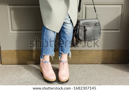 Street fashion set: woman's legs without socks, pink fancy boots shoes and blue denim and mint jacket on outdoor architecture background