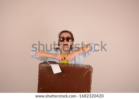 joyful woman in sunglasses going on vacation holds a suitcase on a light background