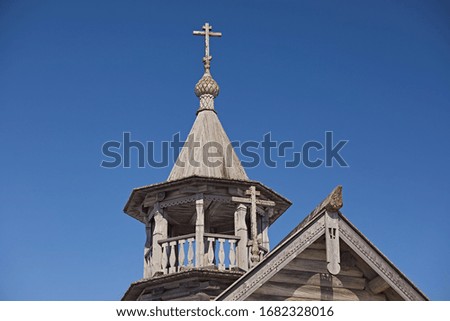Old wooden church with a bell tower, domed shingle and a cross against the blue sky. Traditional orthodox architecture of the north of Russia