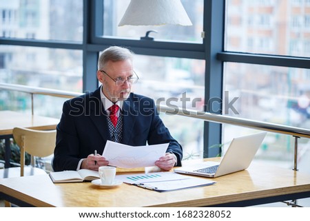 Adult male mentor, director, businessman in glasses and a suit studying documents while sitting at the table. Working day concept
