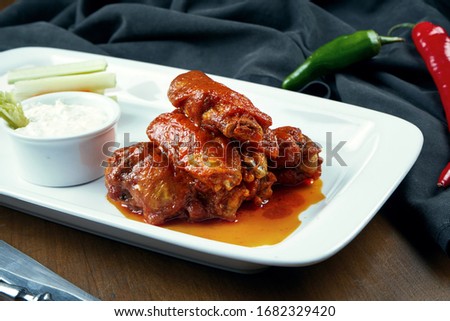 Great beer snack - spicy baked buffalo wings. BBQ wings with garnish of salad on white plate. Close up. Pub food