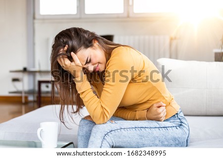 Young sick woman with hands holding pressing her crotch lower abdomen. Medical or gynecological problems, healthcare concept. Young woman suffering from abdominal pain while sitting on sofa at home Royalty-Free Stock Photo #1682348995