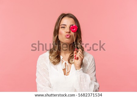 Spring, happiness and celebration concept. Close-up portrait of feminine lovely blond girl in white dress, folding lips in kiss and holding carton stick, partying having fun, stand pink background