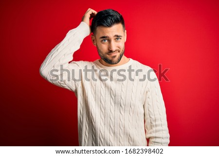 Young handsome man wearing casual white sweater standing over isolated red background confuse and wonder about question. Uncertain with doubt, thinking with hand on head. Pensive concept.