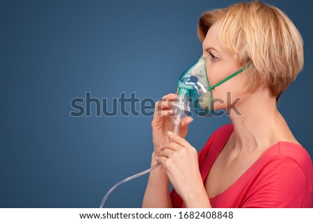 Mature blonde woman wearing oxigen mask standing isolated on blue background coronavirus concept looking forward pensive side view copy space for text or product Royalty-Free Stock Photo #1682408848