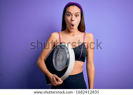 Young beautiful slim sporty girl doing sport wearing sportswear holding weight machine scared in shock with a surprise face, afraid and excited with fear expression